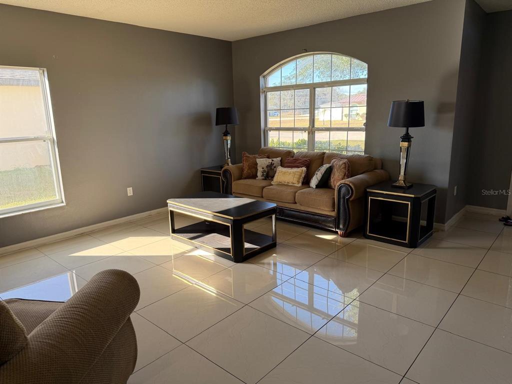 A living room features light tile flooring, a brown sofa, and a large arched window — 1403 KISSIMMEE COURT, KISSIMMEE, FL