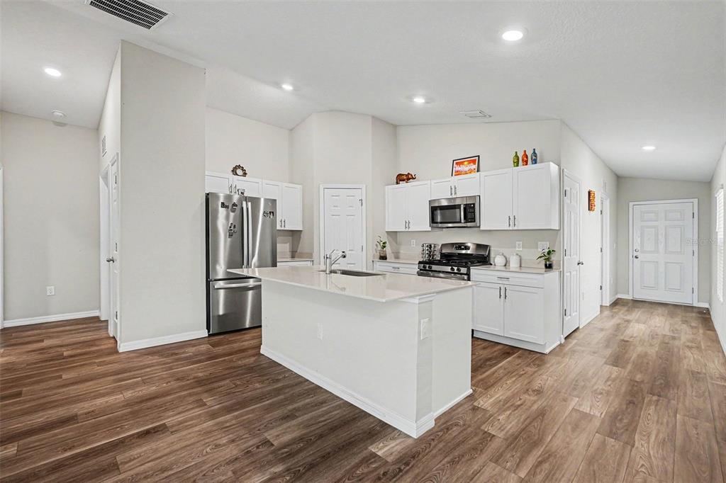 A modern kitchen features white cabinetry, stainless steel appliances, a center island, and wood-look flooring — 14919 STERLING SPUR AVENUE, LITHIA, FL