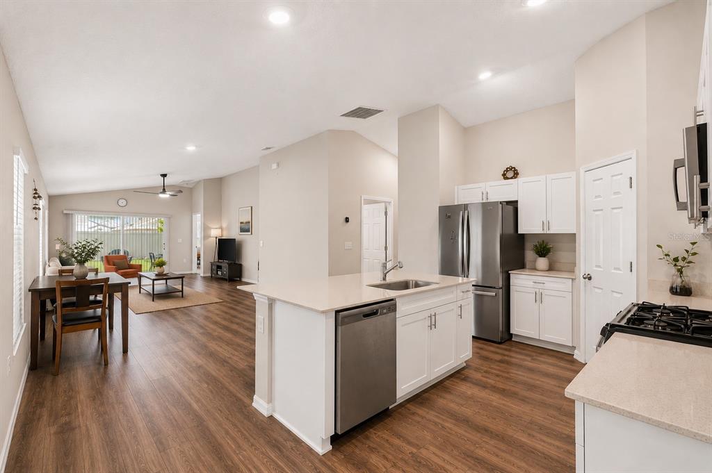 An open-concept kitchen with white cabinets and a center island overlooks a dining and living area — 14919 STERLING SPUR AVENUE, LITHIA, FL