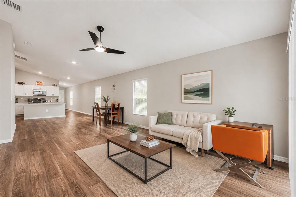 An open-concept living and dining area with wood-look flooring, a white sofa, and kitchen — 14919 STERLING SPUR AVENUE, LITHIA, FL