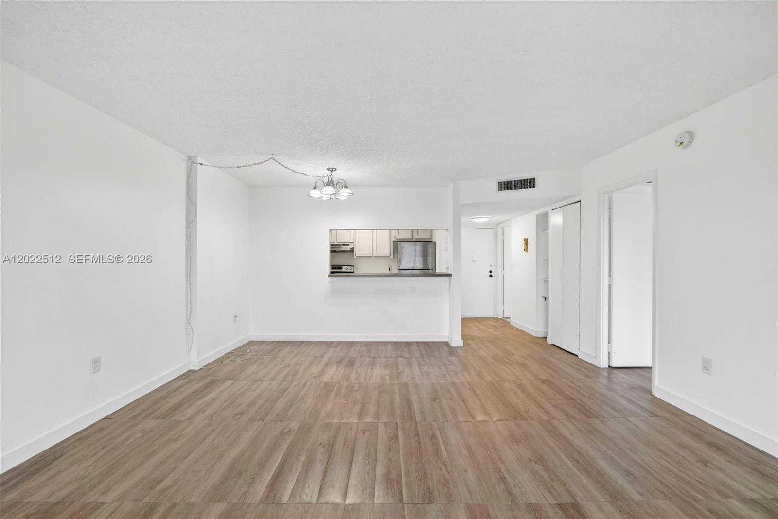 An empty living area features wood-look flooring, white walls, and a kitchen pass-through window — 4174 Inverrary Drive # 706, Lauderhill FL 33319, LAUDERHILL, FL