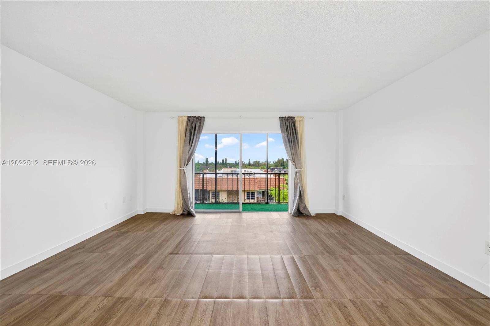 An empty room with wood-look flooring and a sliding glass door leading to a balcony — 4174 Inverrary Drive # 706, Lauderhill FL 33319, LAUDERHILL, FL