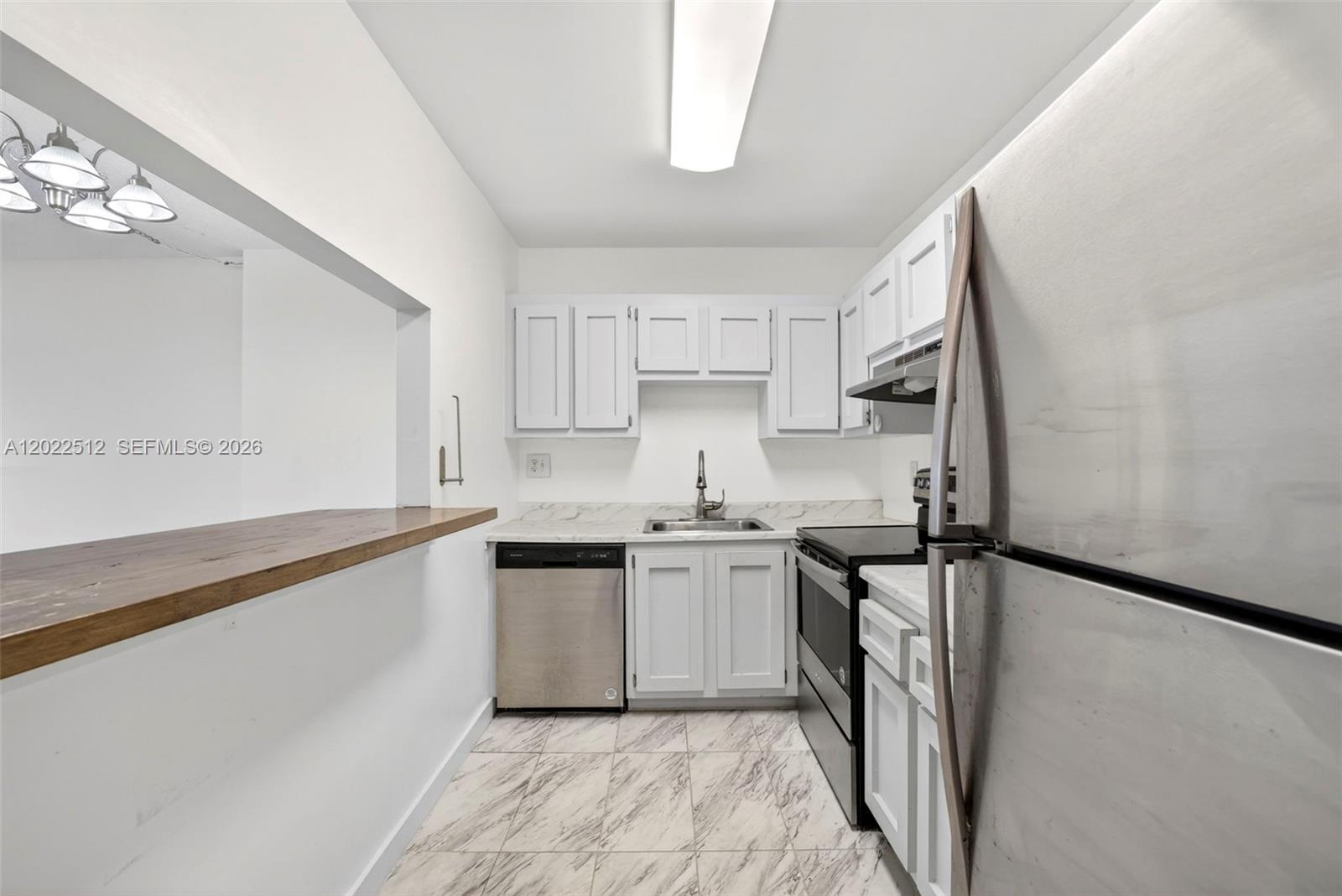 A galley kitchen features white cabinets, stainless steel appliances, and a wood-topped breakfast bar — 4174 Inverrary Drive # 706, Lauderhill FL 33319, LAUDERHILL, FL