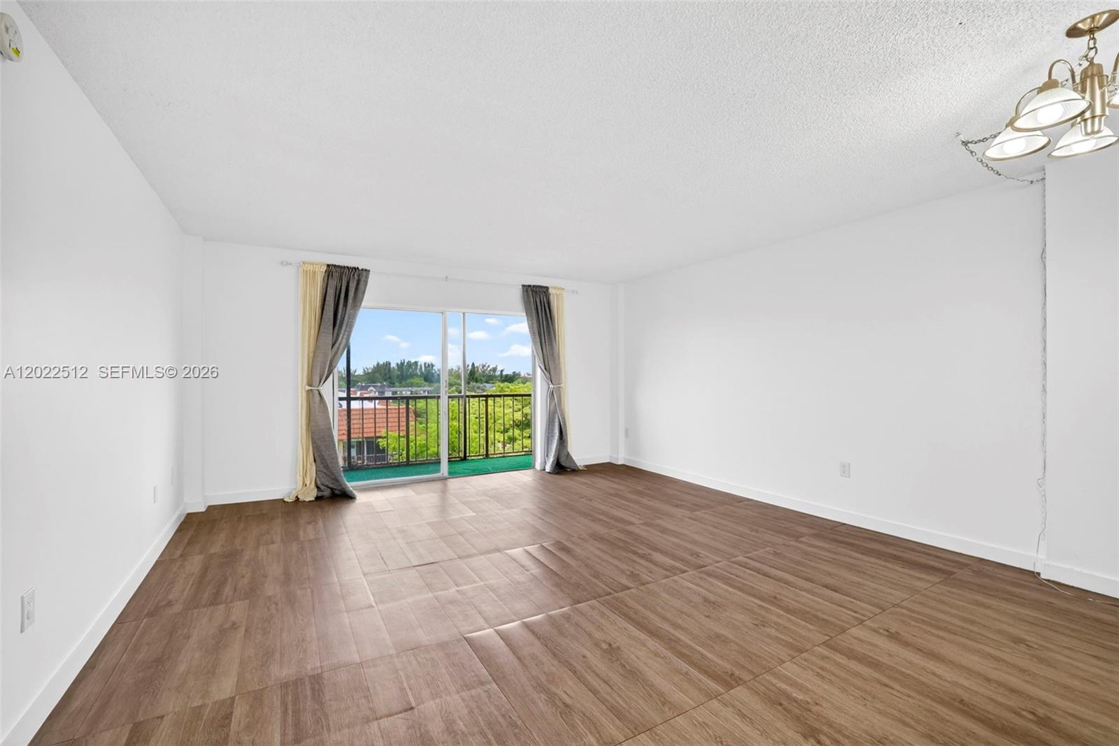 A bright, empty room features wood-look tile flooring, white walls, and a sliding glass balcony door — 4174 Inverrary Drive # 706, Lauderhill FL 33319, LAUDERHILL, FL