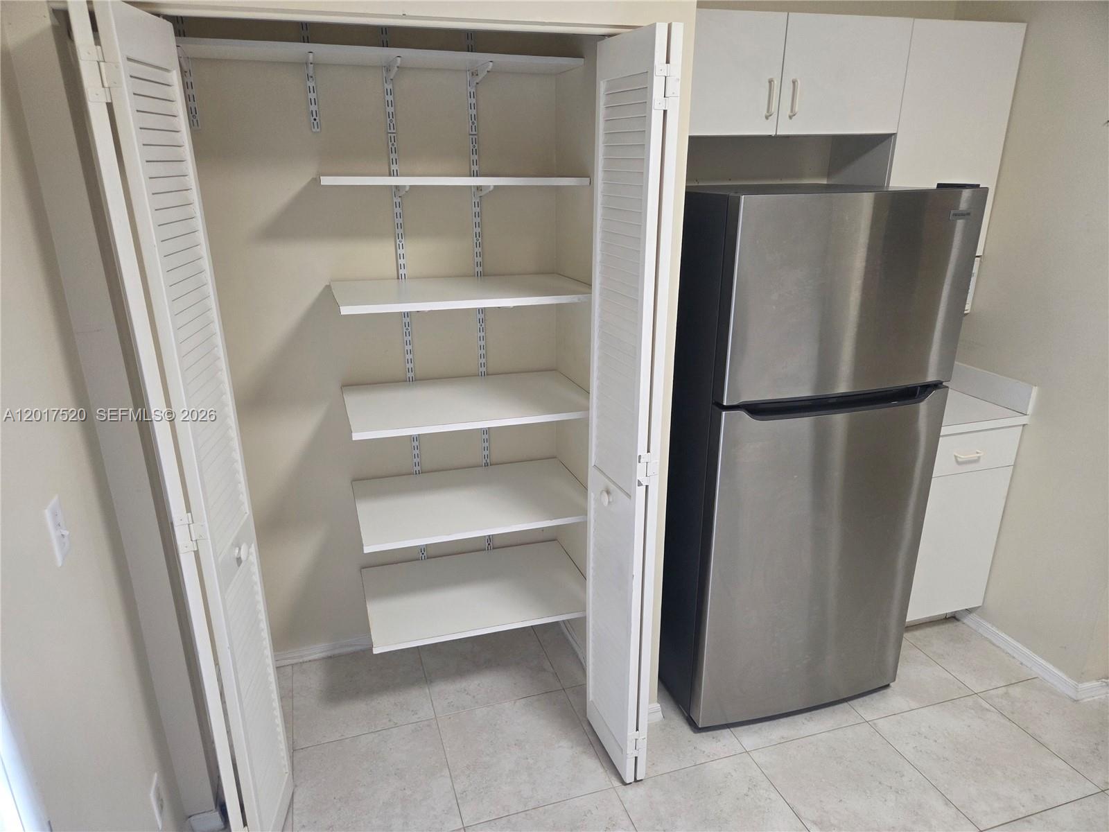 A kitchen pantry with adjustable white shelves stands next to a stainless steel refrigerator — 47 Simonton Cir, Weston FL 33326, WESTON, FL