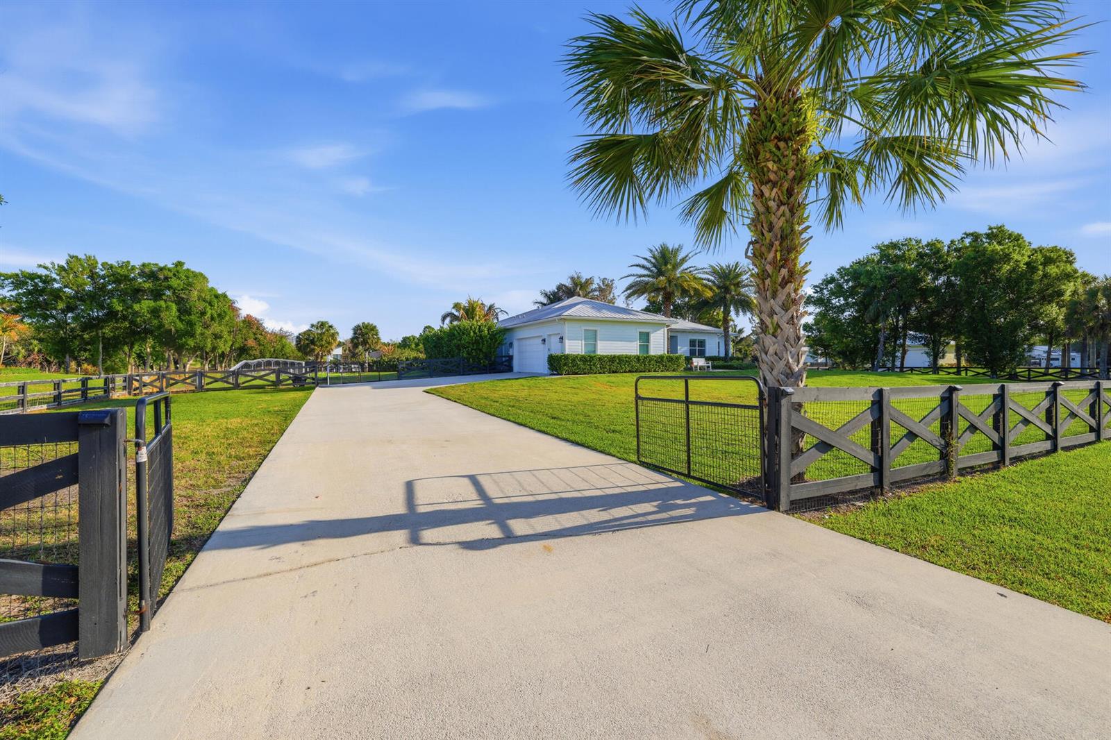 A concrete driveway leads toward a light-colored house behind a black wooden fence — 9301 154th Road N, Jupiter FL 33478, JUPITER, FL