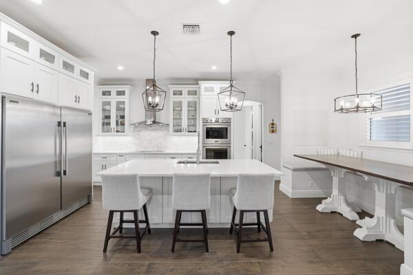 A white kitchen features a large center island, stainless steel appliances, and dark wood floors — 9301 154th Road N, Jupiter FL 33478, JUPITER, FL