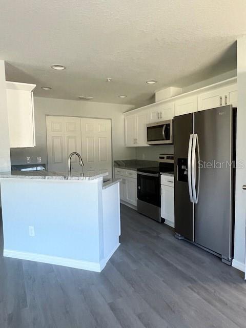 A kitchen features white cabinets, stainless steel appliances, a breakfast bar, and gray wood flooring — 4076 OAK LOOP UNIT 4076, MULBERRY, FL