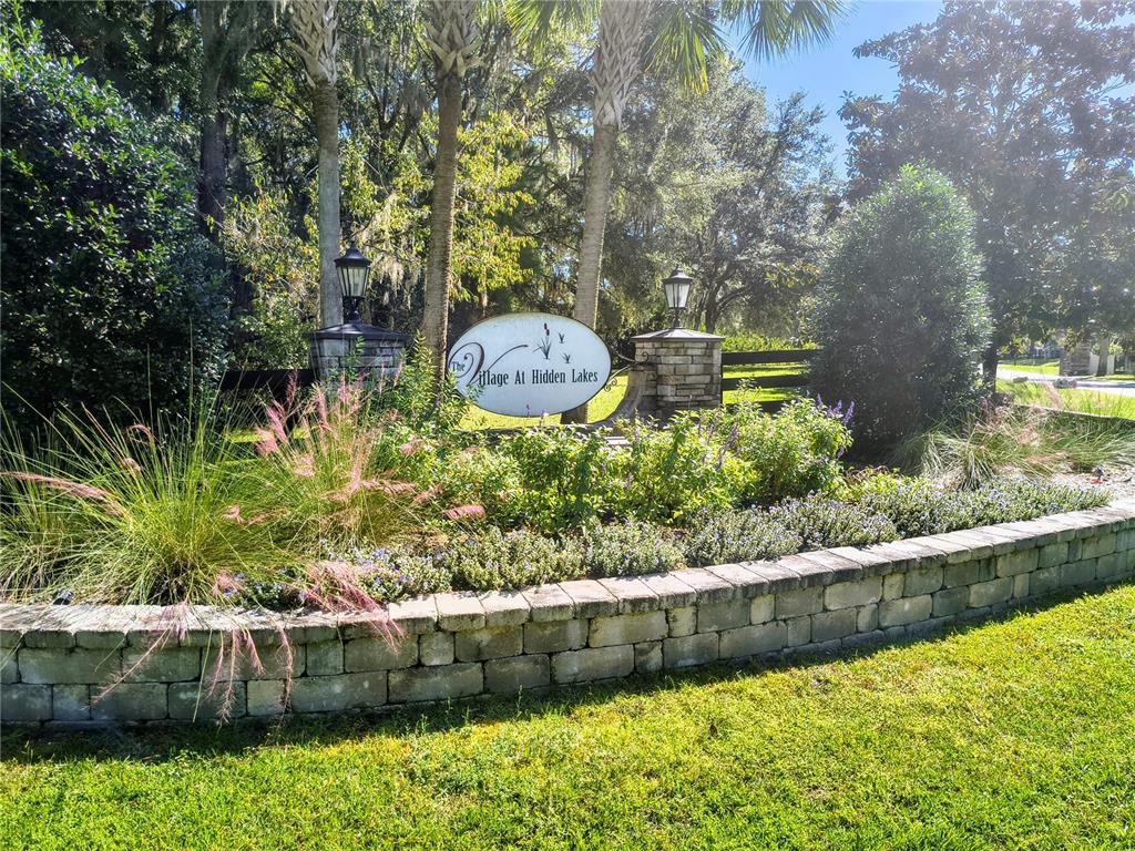 A stone retaining wall surrounds a landscaped garden with a sign for The Village at Hidden Lakes — NW 148TH LANE, WILLISTON, FL