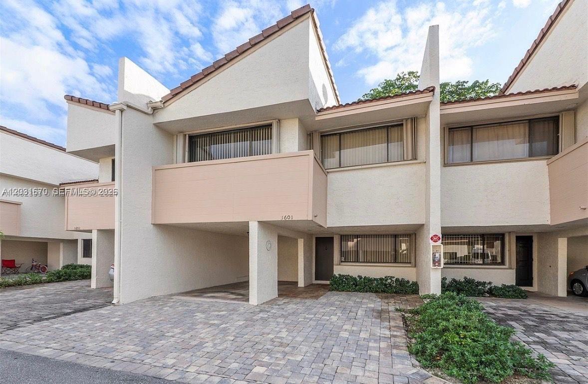 A two-story townhouse features a paved driveway, a covered carport, and a balcony — CORAL SPRINGS, FL