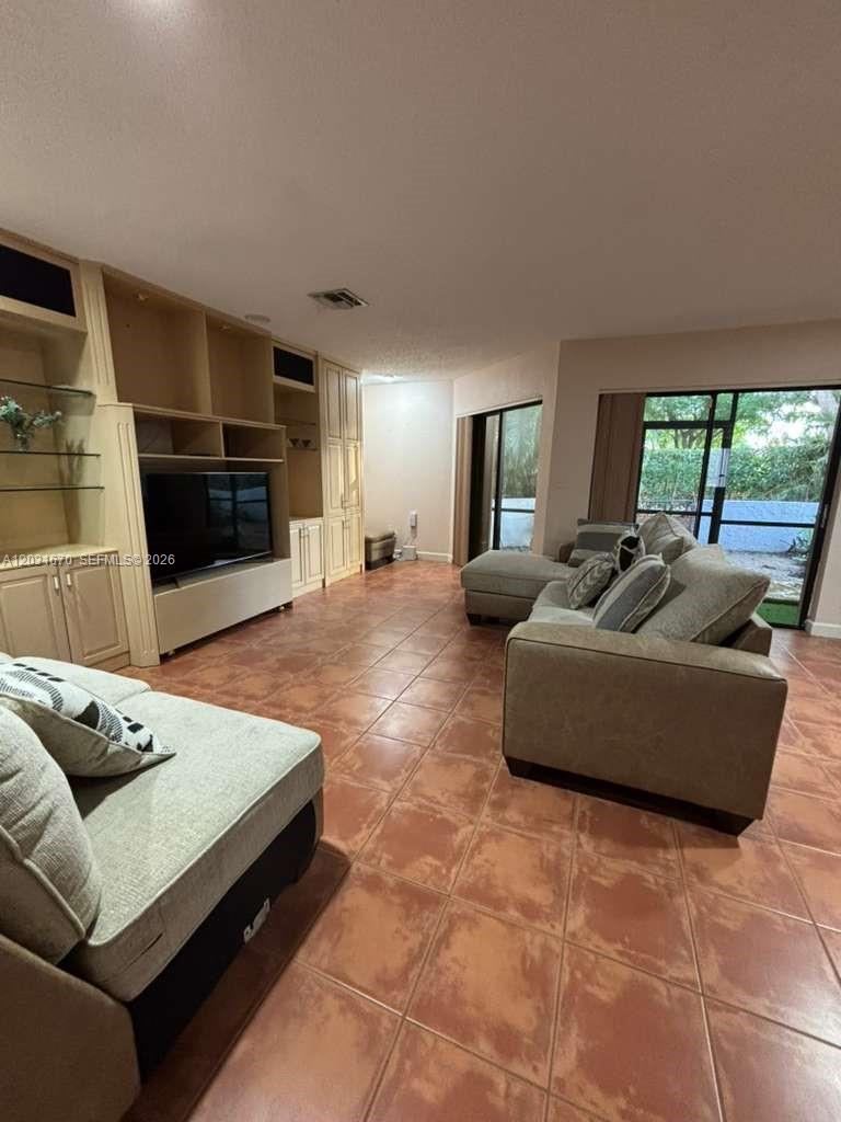 A living room features light-colored built-in shelving, a television, tile flooring, and a sectional sofa — CORAL SPRINGS, FL