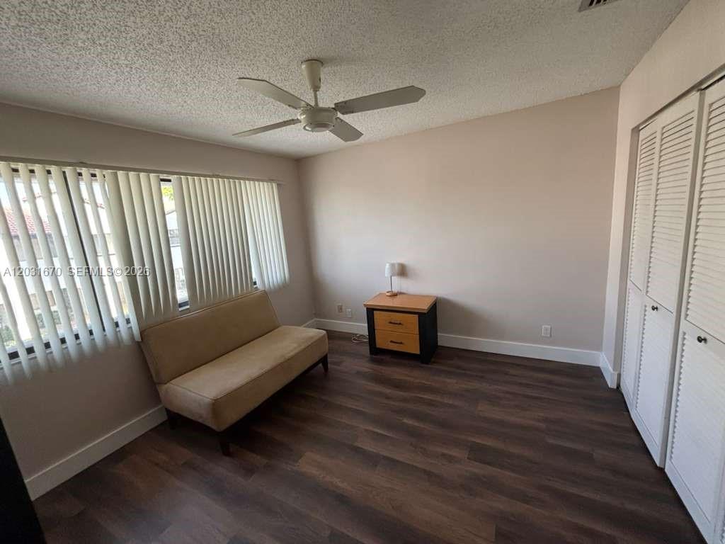 A bedroom features a tan sofa, a small wooden nightstand, and white louvered closet doors — CORAL SPRINGS, FL