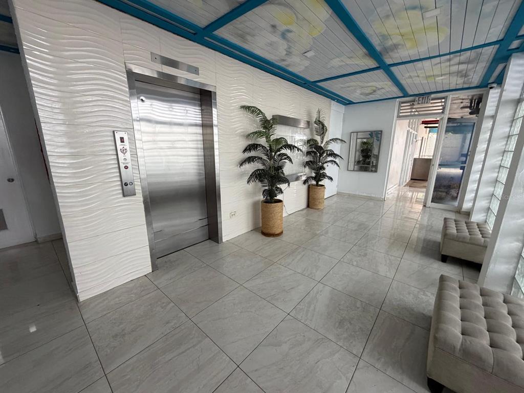 A modern elevator lobby features white textured walls, tile flooring, potted plants, and a ceiling mural — 37 ISLA VERDE AVENUE UNIT 4C, CAROLINA, PR