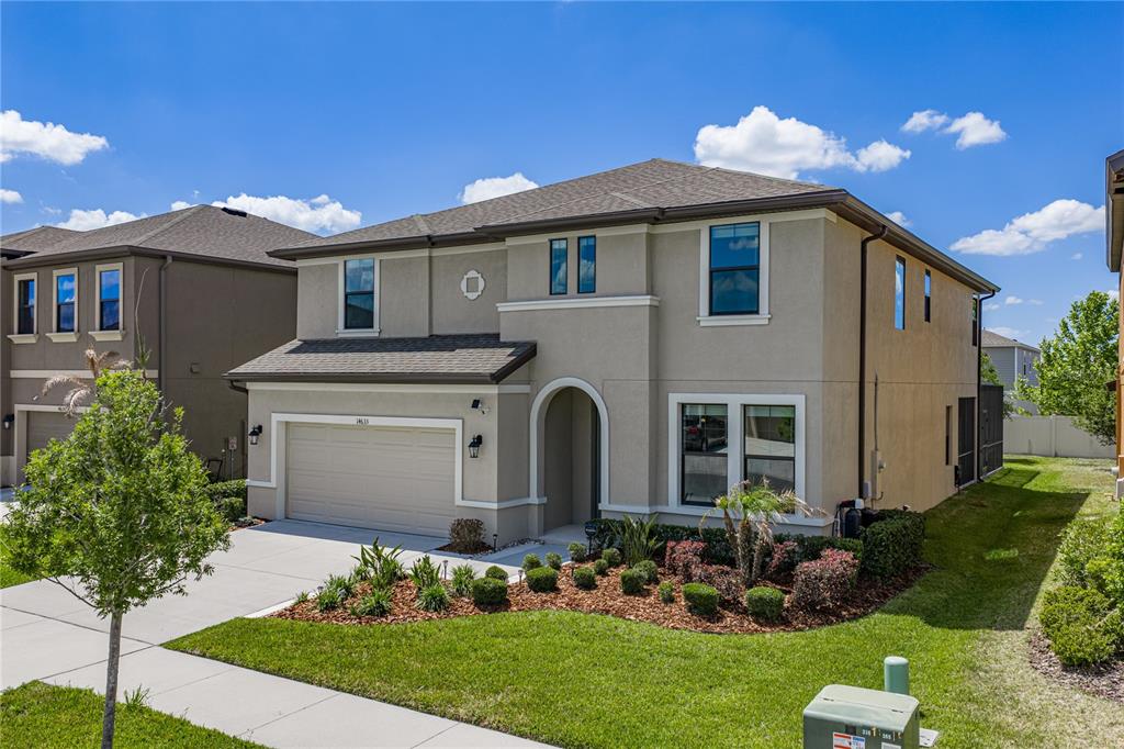 A two-story suburban house with a beige stucco exterior, a two-car garage, and landscaping — 14633 RED CASTLE AVENUE, LITHIA, FL