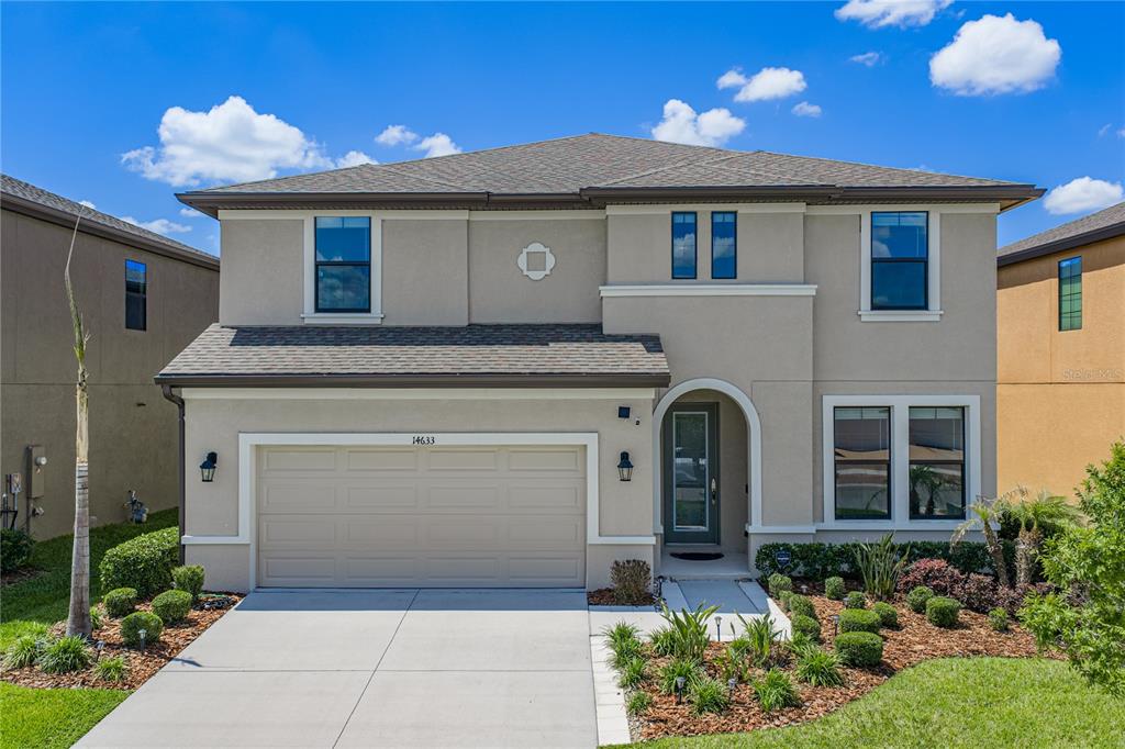 A two-story suburban house with a beige stucco exterior, a two-car garage, and landscaping — 14633 RED CASTLE AVENUE, LITHIA, FL