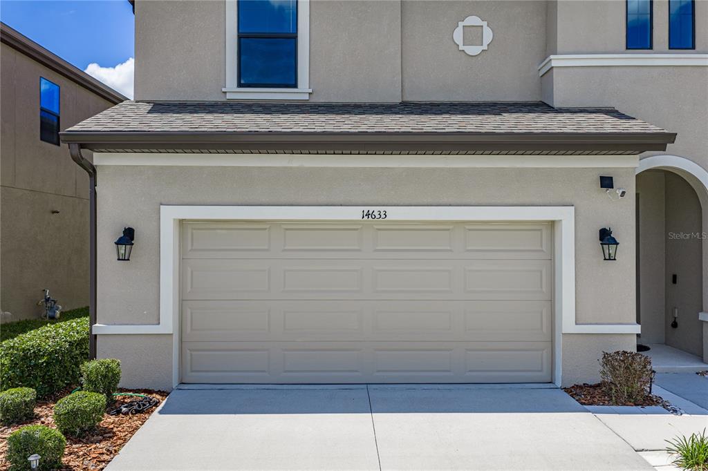 The exterior of a house features a beige two-car garage with a concrete driveway — 14633 RED CASTLE AVENUE, LITHIA, FL