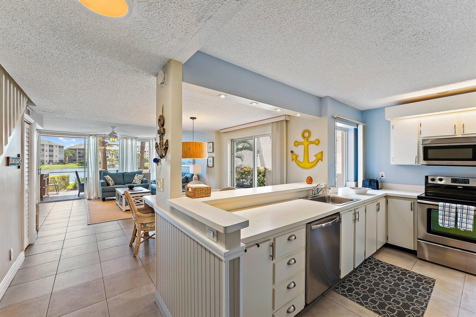 A kitchen with white cabinets and stainless steel appliances overlooks a living area with water views — 353 S Us Highway 1 # A105, Jupiter FL 33477, JUPITER, FL