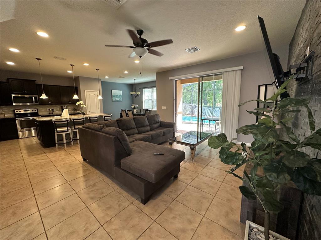 A screened-in swimming pool sits on a brick patio next to a two-story tan house — 1869 NICE COURT, KISSIMMEE, FL