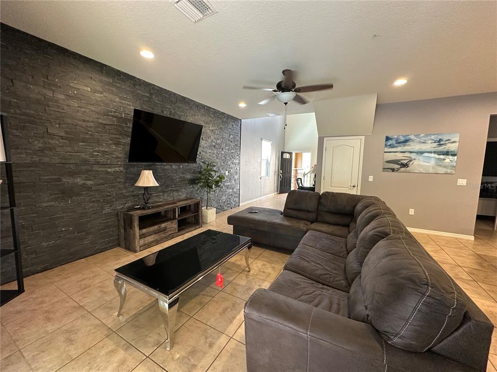 An open-concept living room and kitchen featuring tile floors, a sectional sofa, and pool access — 1869 NICE COURT, KISSIMMEE, FL