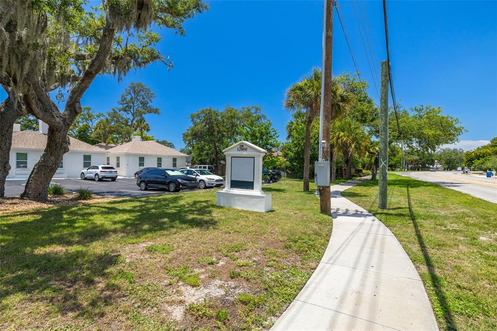 A white building with a parking lot and a sign stands next to a sidewalk — 12800 INDIAN ROCKS ROAD, LARGO, FL