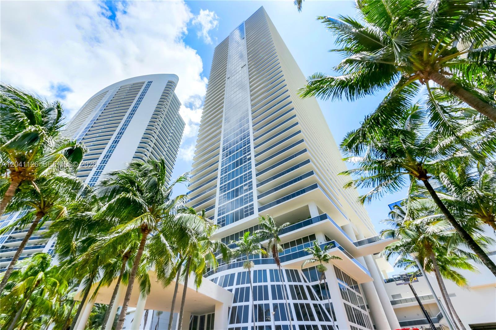Low-angle view of two modern high-rise residential towers framed by palm trees — HALLANDALE BEACH, FL