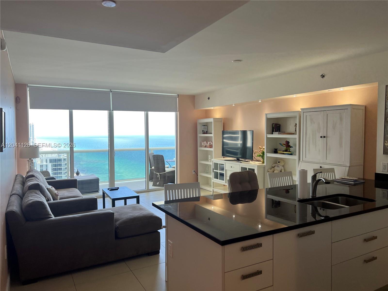 An open-concept living room and kitchen area features a balcony with ocean views — HALLANDALE BEACH, FL