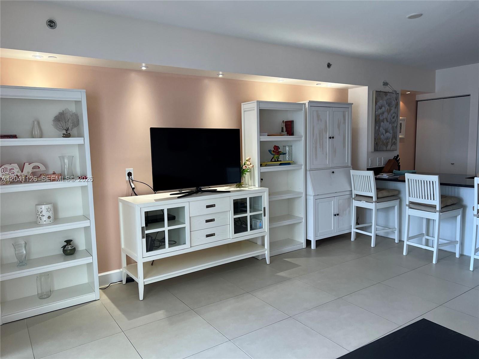 A living room features a pink accent wall, white shelving, a television console, and bar stools — HALLANDALE BEACH, FL