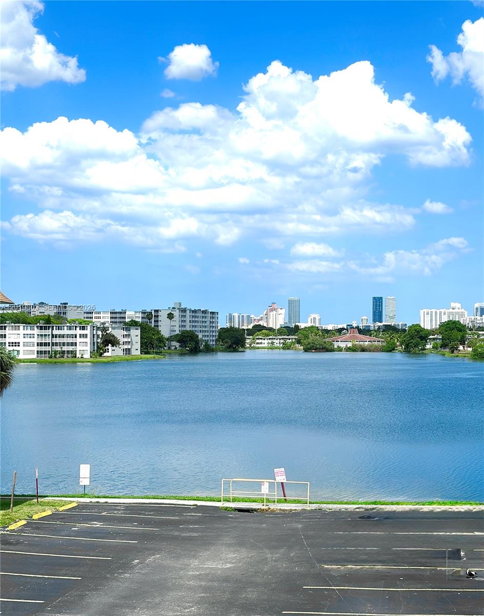 A parking lot overlooks a calm lake with apartment buildings and a city skyline beyond — 18601 NE 14th ave # 301, Miami FL 33179, MIAMI, FL