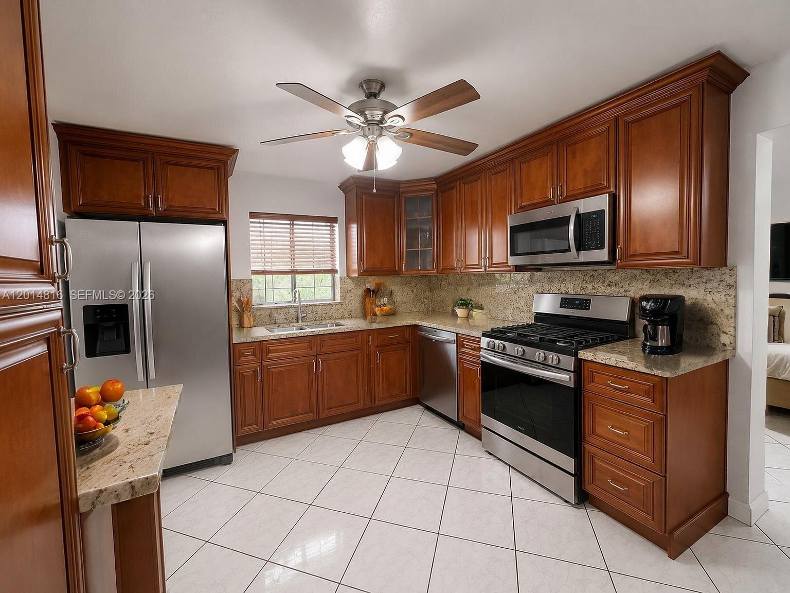 A kitchen features wood cabinets, stainless steel appliances, granite countertops, and white tile flooring — 951 E 18th St, Hialeah FL 33013, HIALEAH, FL