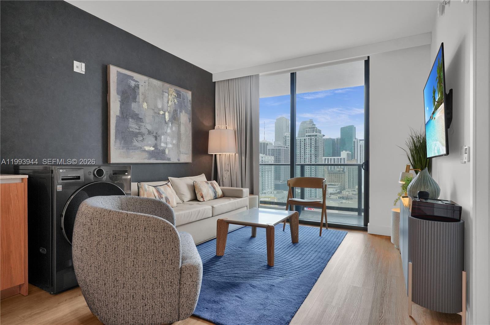A living room features a sofa, blue rug, and a washing machine near the balcony window — 159 NE 6th St # 1809, Miami FL 33132, MIAMI, FL
