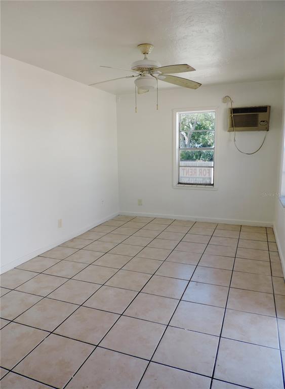 An empty room with white walls, beige tile flooring, a ceiling fan, and a window unit — 12127 GULF BOULEVARD UNIT 1, TREASURE ISLAND, FL