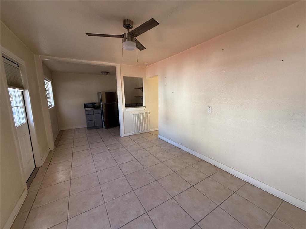 A room with light-colored tile flooring, a ceiling fan, and a view into a kitchen — 12127 GULF BOULEVARD UNIT 1, TREASURE ISLAND, FL