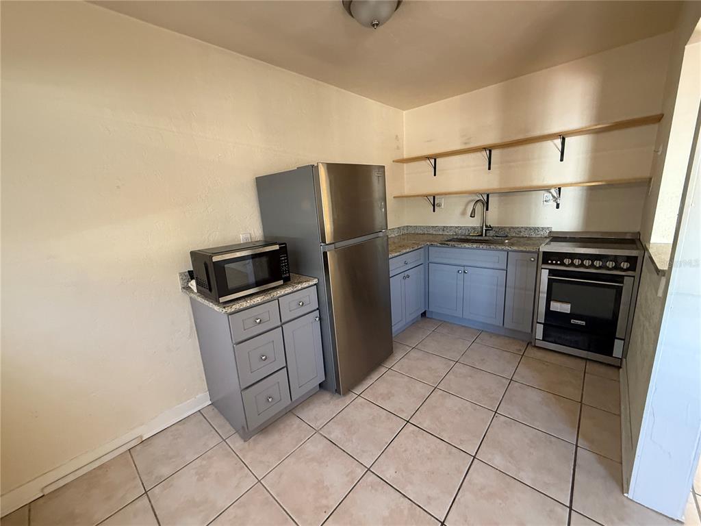 A kitchen features gray cabinets, stainless steel appliances, open shelving, and light-colored tile flooring — 12127 GULF BOULEVARD UNIT 1, TREASURE ISLAND, FL