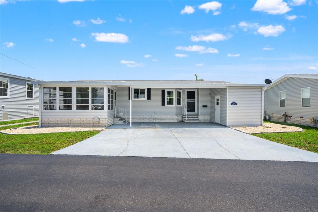 A single-story manufactured home with light gray siding, a concrete driveway, and a carport — 116 MOUNT ISLE AVENUE NE UNIT 116, ST PETERSBURG, FL