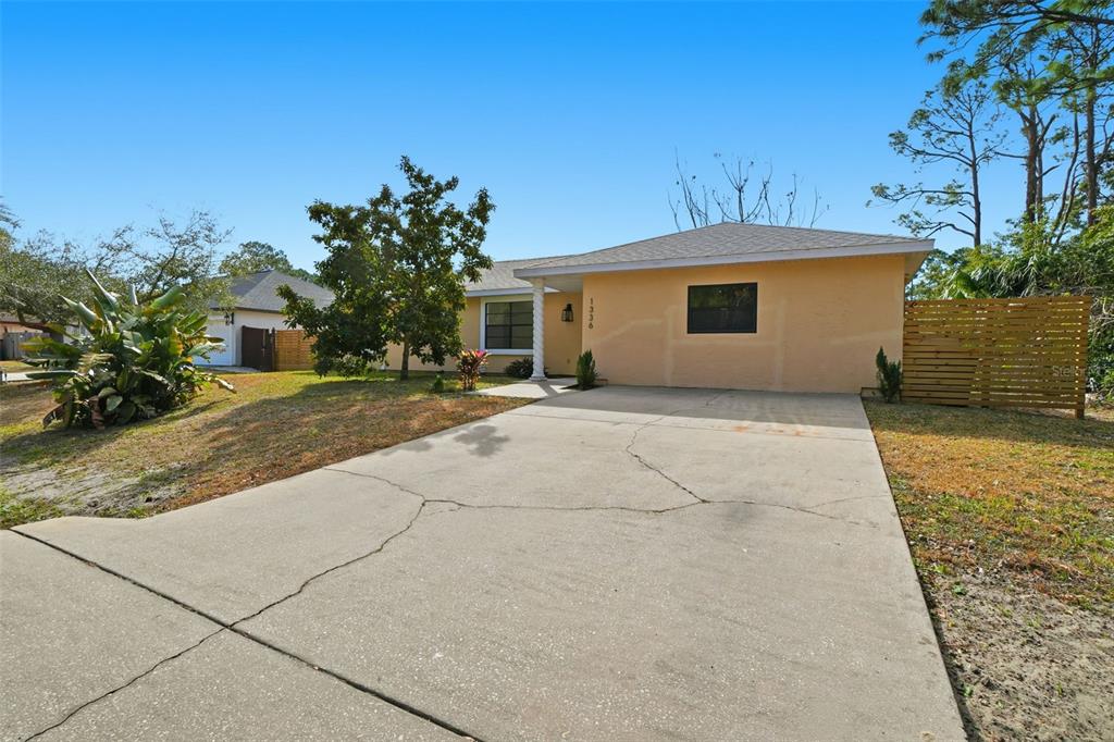 A single-story house with a tan stucco exterior, a concrete driveway, and a wooden fence — 1336 GINGOLD STREET NW, PALM BAY, FL