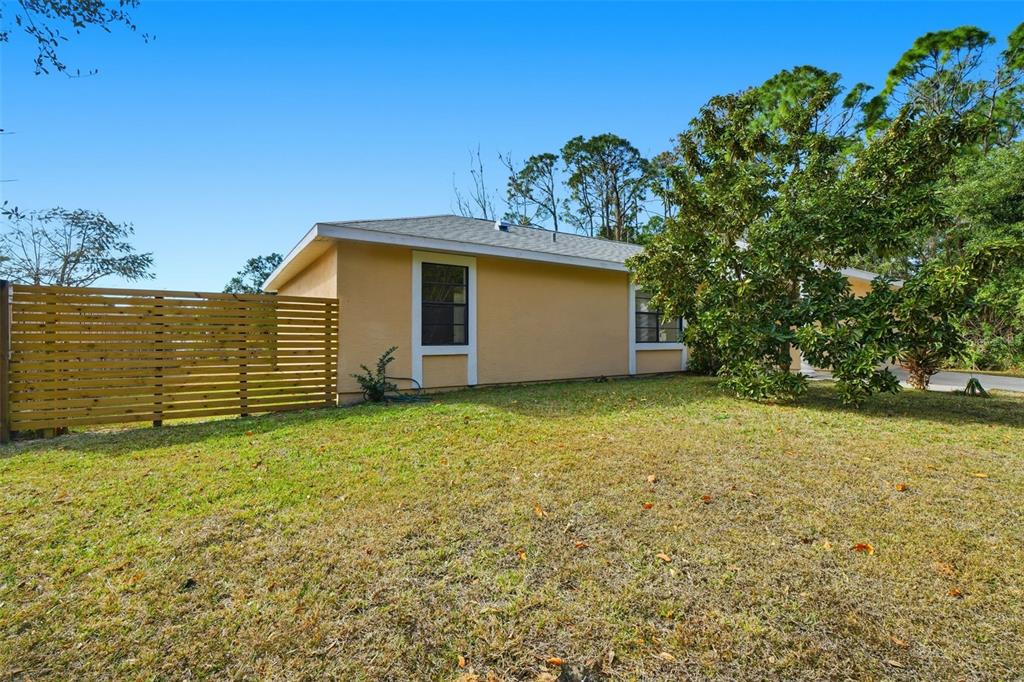 The exterior of a tan house features a wooden privacy fence and a large tree — 1336 GINGOLD STREET NW, PALM BAY, FL