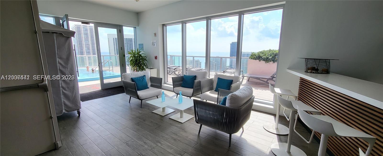 A modern living area features gray armchairs, a white coffee table, and floor-to-ceiling windows — 2602 E Hallandale Beach Blvd # R306, Hallandale Beach FL 33009, HALLANDALE BEACH, FL