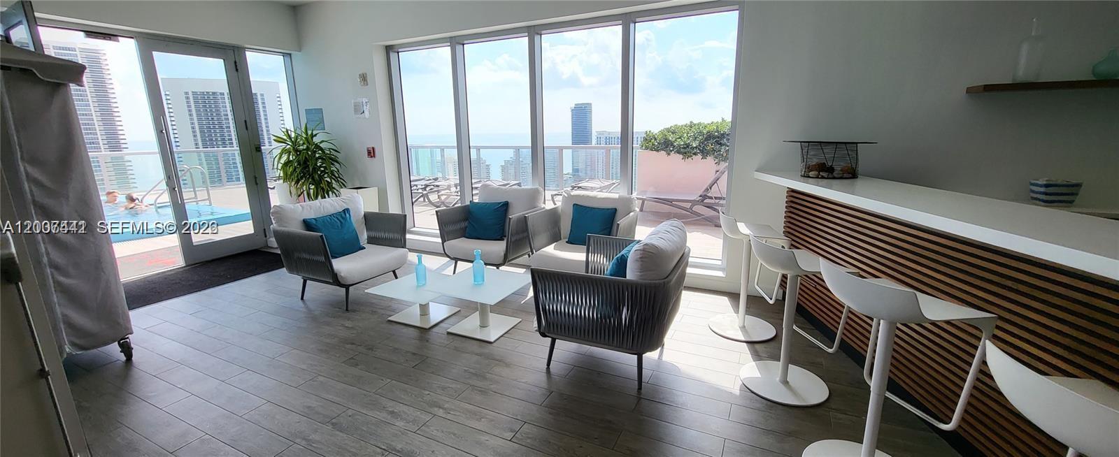 A lounge area features modern seating, a bar counter, and floor-to-ceiling windows overlooking a pool — 2602 E Hallandale Beach Blvd # R306, Hallandale Beach FL 33009, HALLANDALE BEACH, FL