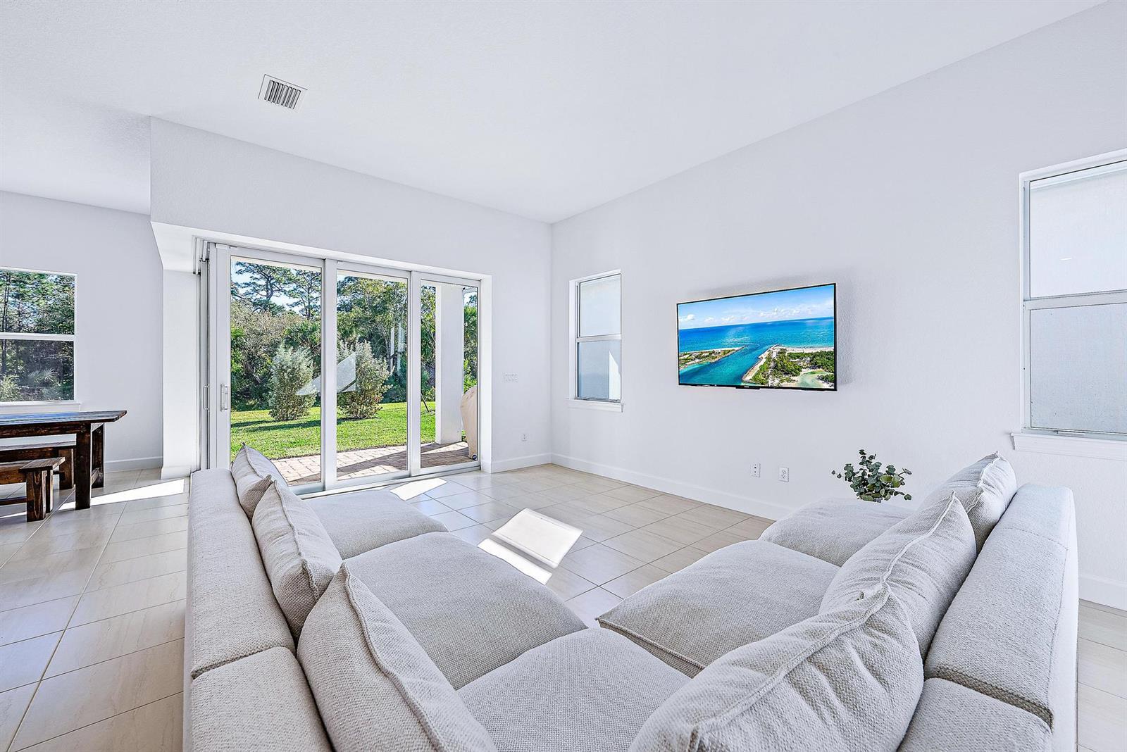 A bright living room features a large sectional sofa, a wall-mounted television, and sliding doors — 9775 SW Meridian Way, Stuart FL 34997, STUART, FL