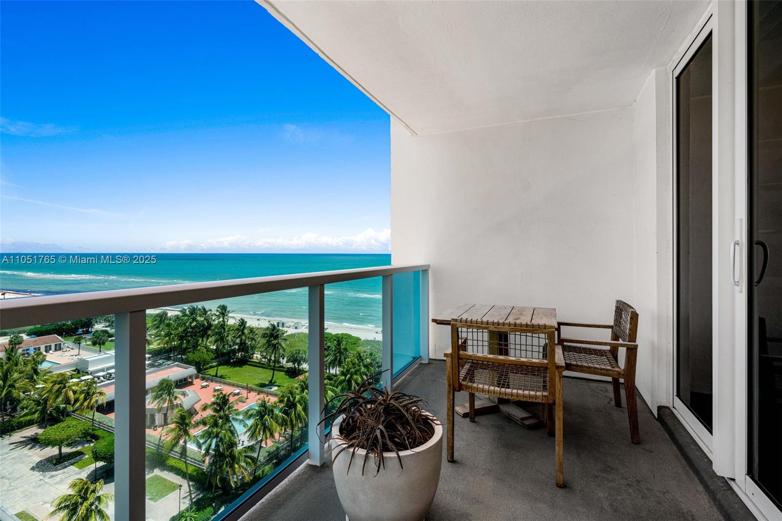 A balcony with a small wooden table, two chairs, a potted plant, and ocean views — 102 24th St # 1115, Miami Beach FL 33139, MIAMI BEACH, FL