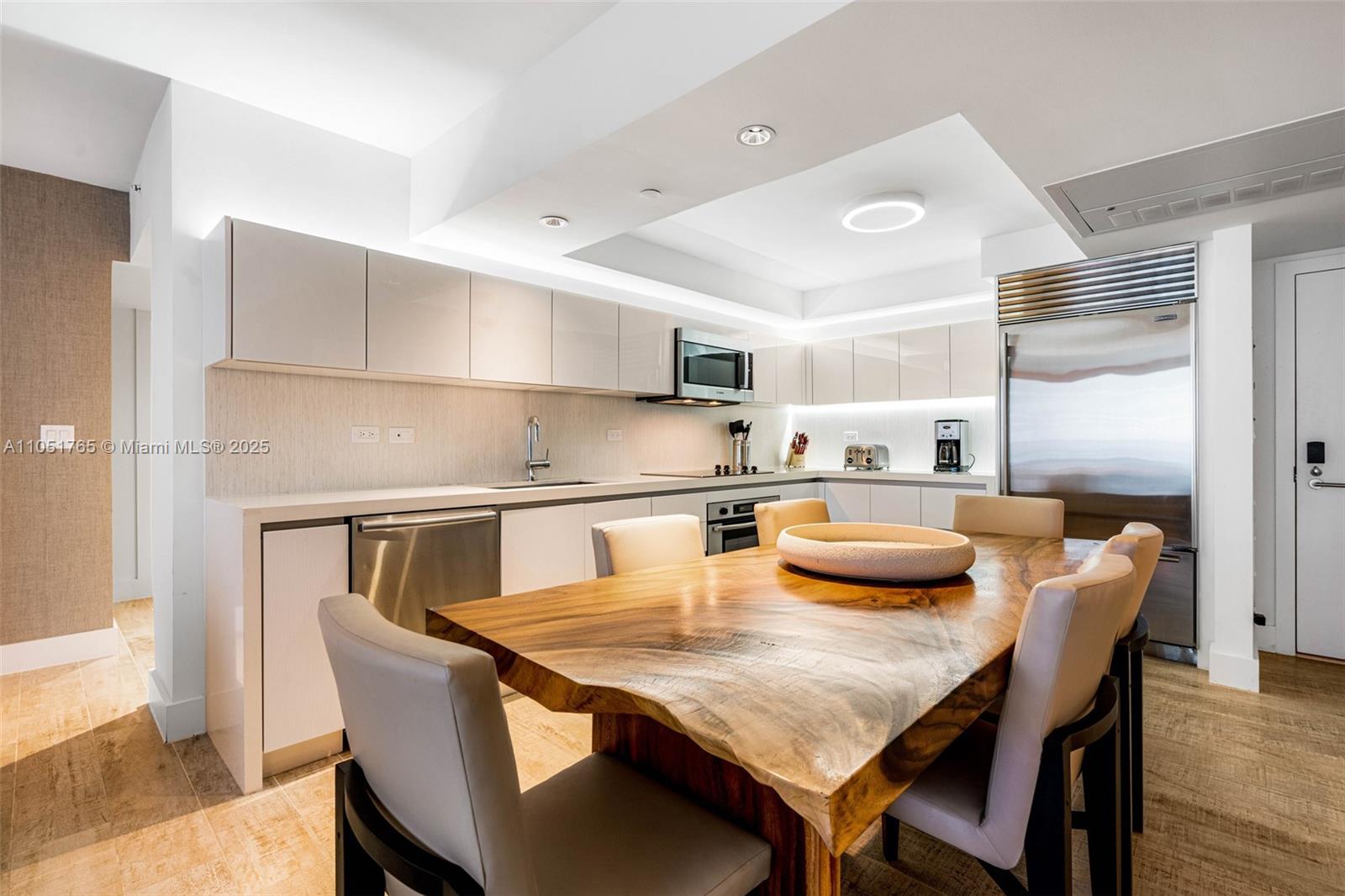 A modern kitchen features white cabinetry, stainless steel appliances, and a large live-edge wooden table — 102 24th St # 1115, Miami Beach FL 33139, MIAMI BEACH, FL