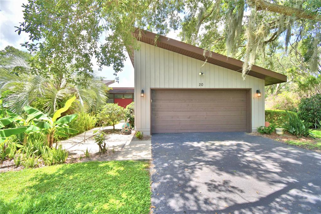 A single-story house with a brown garage door, light siding, and lush tropical landscaping — 20 NOTTINGHAM WAY, HAINES CITY, FL