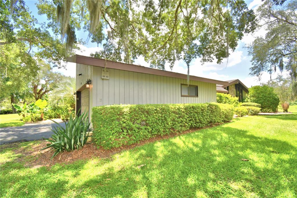 A side view of a house exterior with gray vertical siding, a hedge, and trees — 20 NOTTINGHAM WAY, HAINES CITY, FL