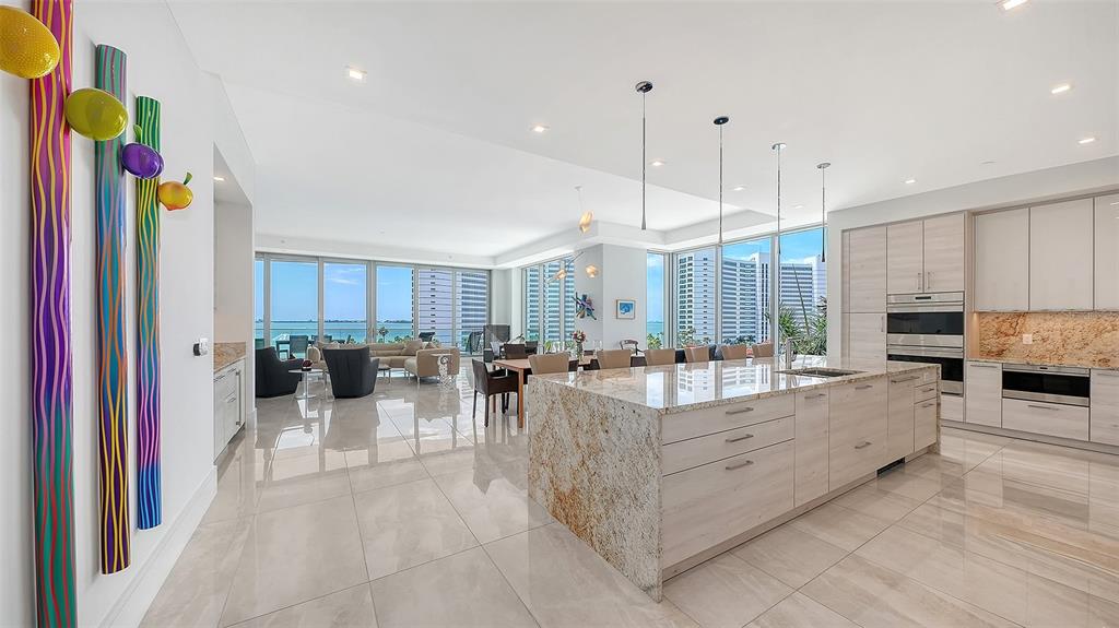 A modern kitchen with a granite island overlooks a living area and a coastal view — 401 QUAY COMMONS UNIT 505, SARASOTA, FL