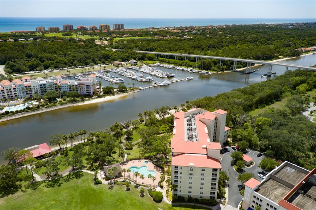 An aerial view shows a waterfront condominium complex with a marina, pool, and bridge — 146 PALM COAST RESORT BOULEVARD UNIT 501, PALM COAST, FL