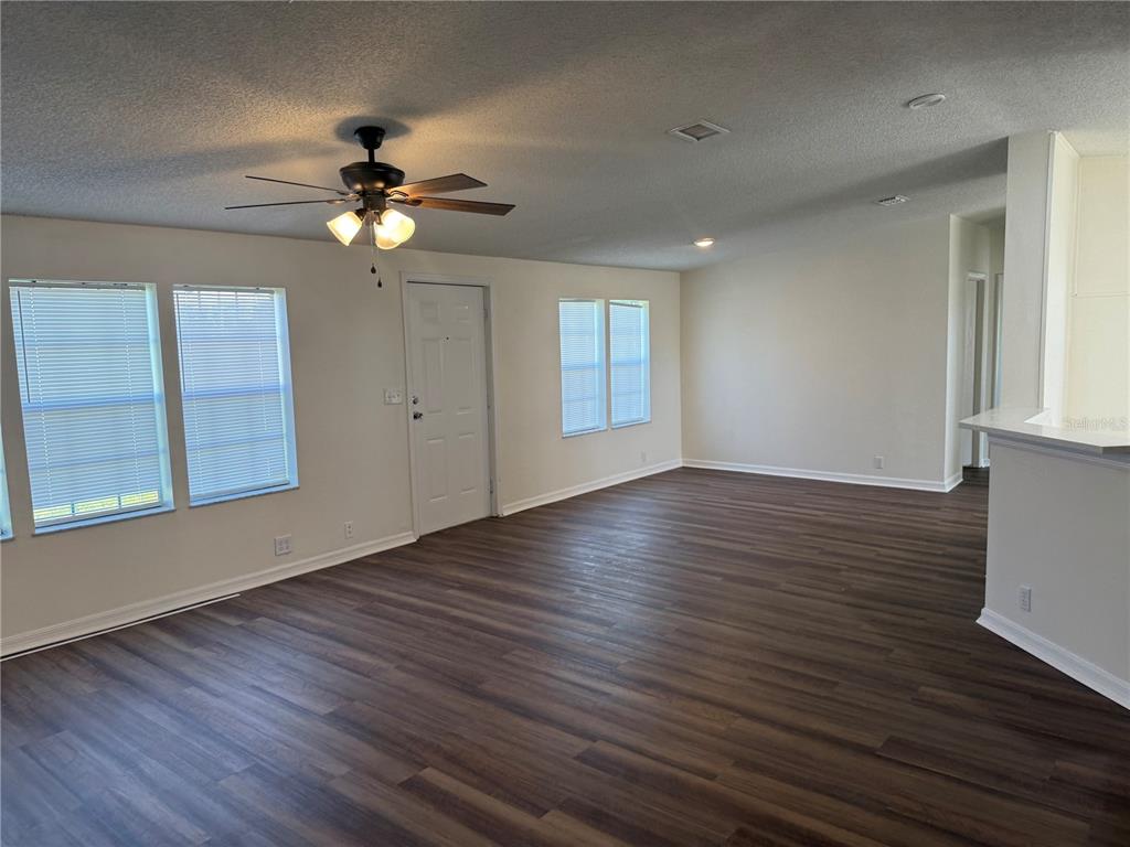 A spacious living room features dark wood-look flooring, white walls, and a ceiling fan — 4795 SCHOONER AVENUE, LAKE WALES, FL
