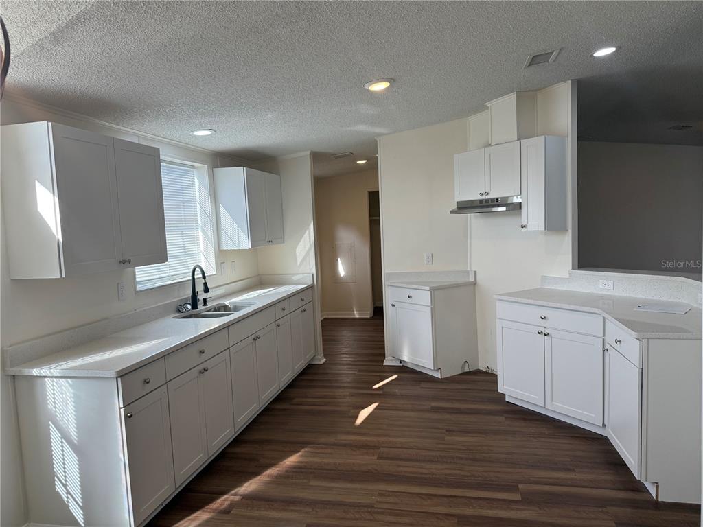 A kitchen features white cabinets, light countertops, and dark wood-look flooring — 4795 SCHOONER AVENUE, LAKE WALES, FL