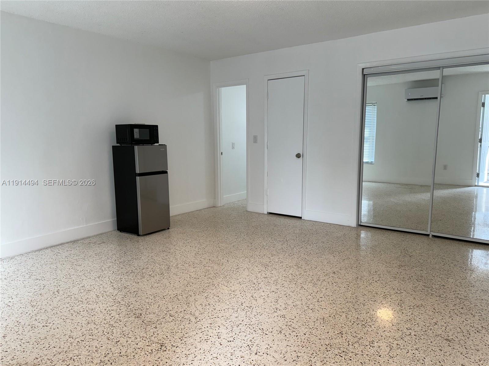 A room with white walls, a terrazzo floor, a small refrigerator, and mirrored closet doors — 3144 NW 29th St # 2, Miami FL 33142, MIAMI, FL