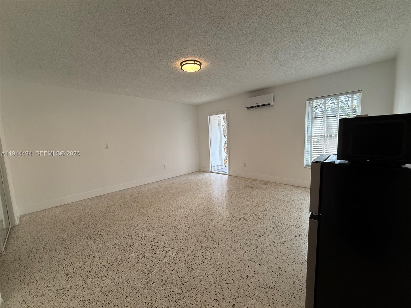 An empty room features white walls, a speckled floor, a ceiling light, and a wall-mounted AC — 3144 NW 29th St # 2, Miami FL 33142, MIAMI, FL