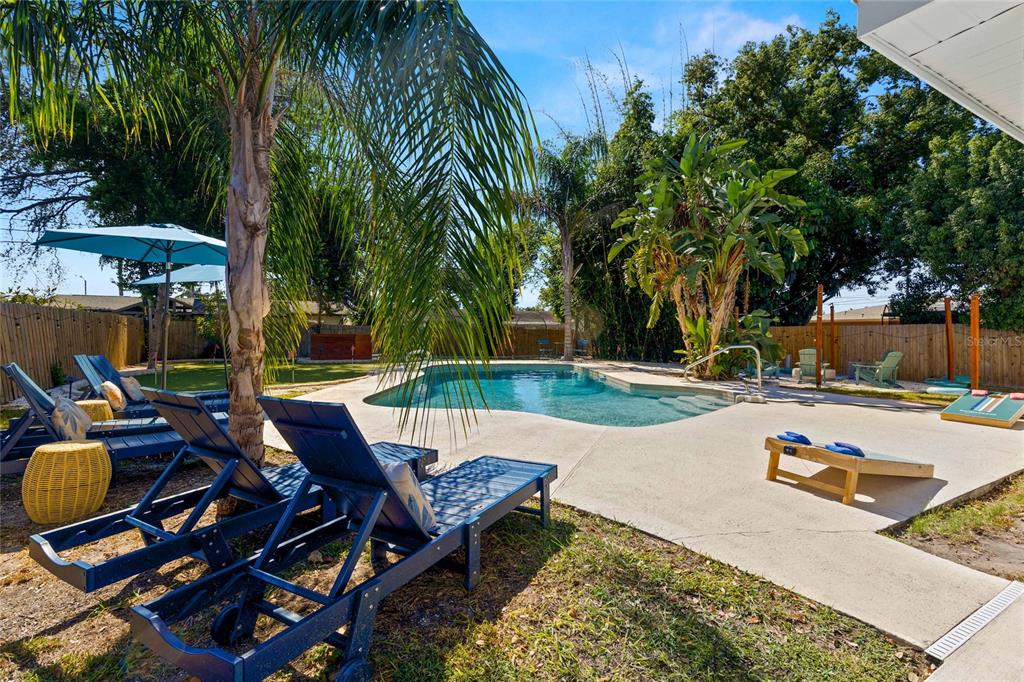 A backyard features a swimming pool, lounge chairs, a palm tree, and a cornhole game — 13672 88TH AVENUE, SEMINOLE, FL